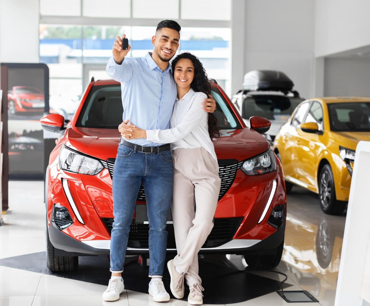 Couple holding car keys in front of a new vehicle at a dealership